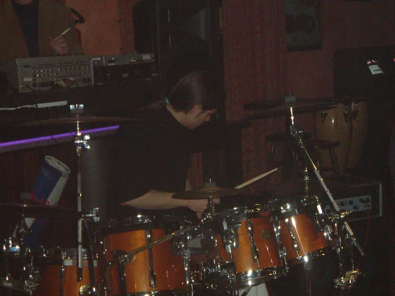 Fabio D’Amico playing a natural-wood drum kit in a dimly lit rehearsal room