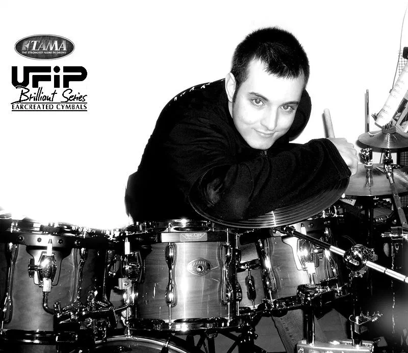 Black-and-white promo photo of Fabio D’Amico behind a TAMA drum kit, with TAMA and UFIP Brilliant Series logos